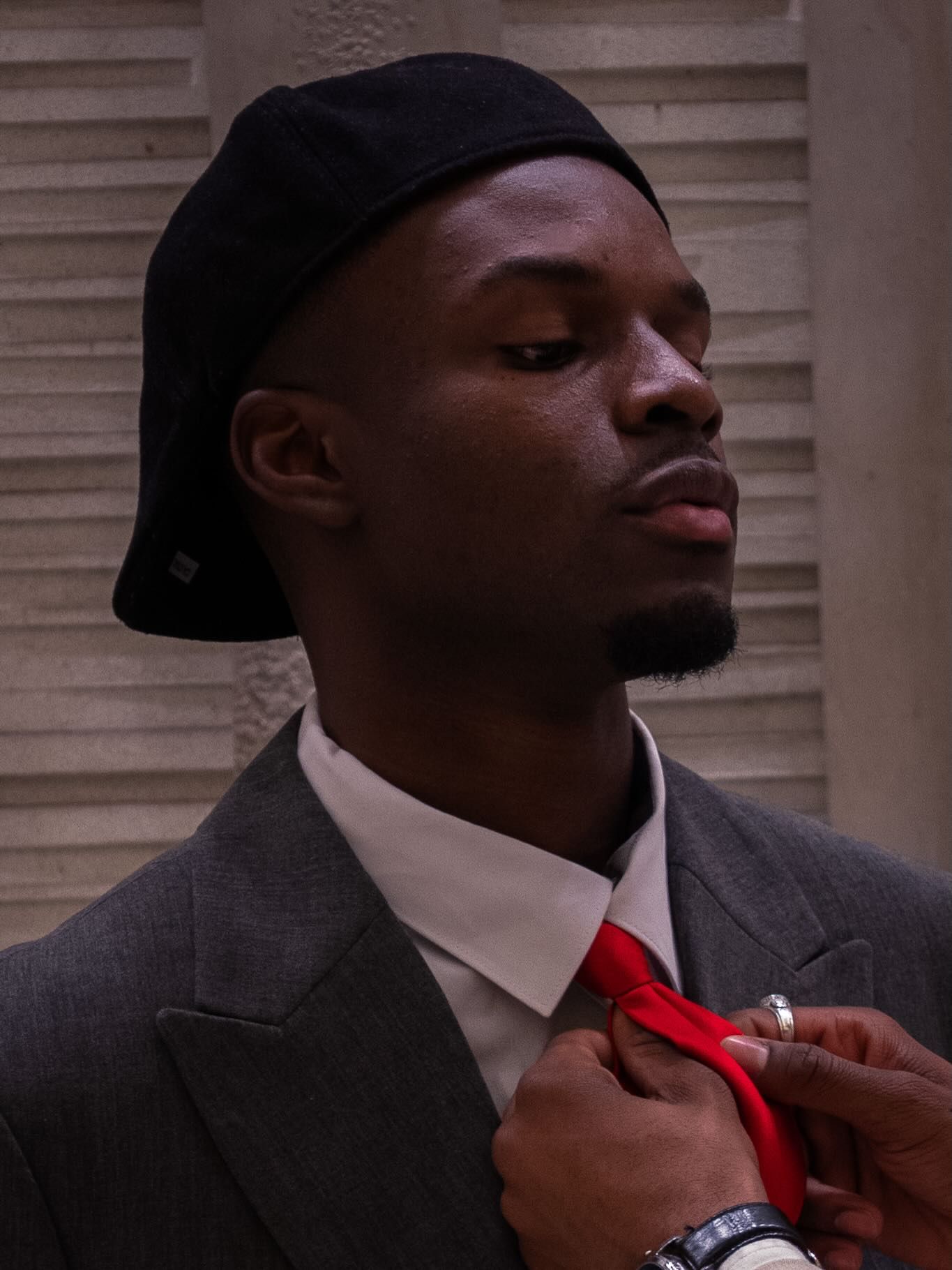 Graël en béret noir et costume gris, nouant une cravate rouge