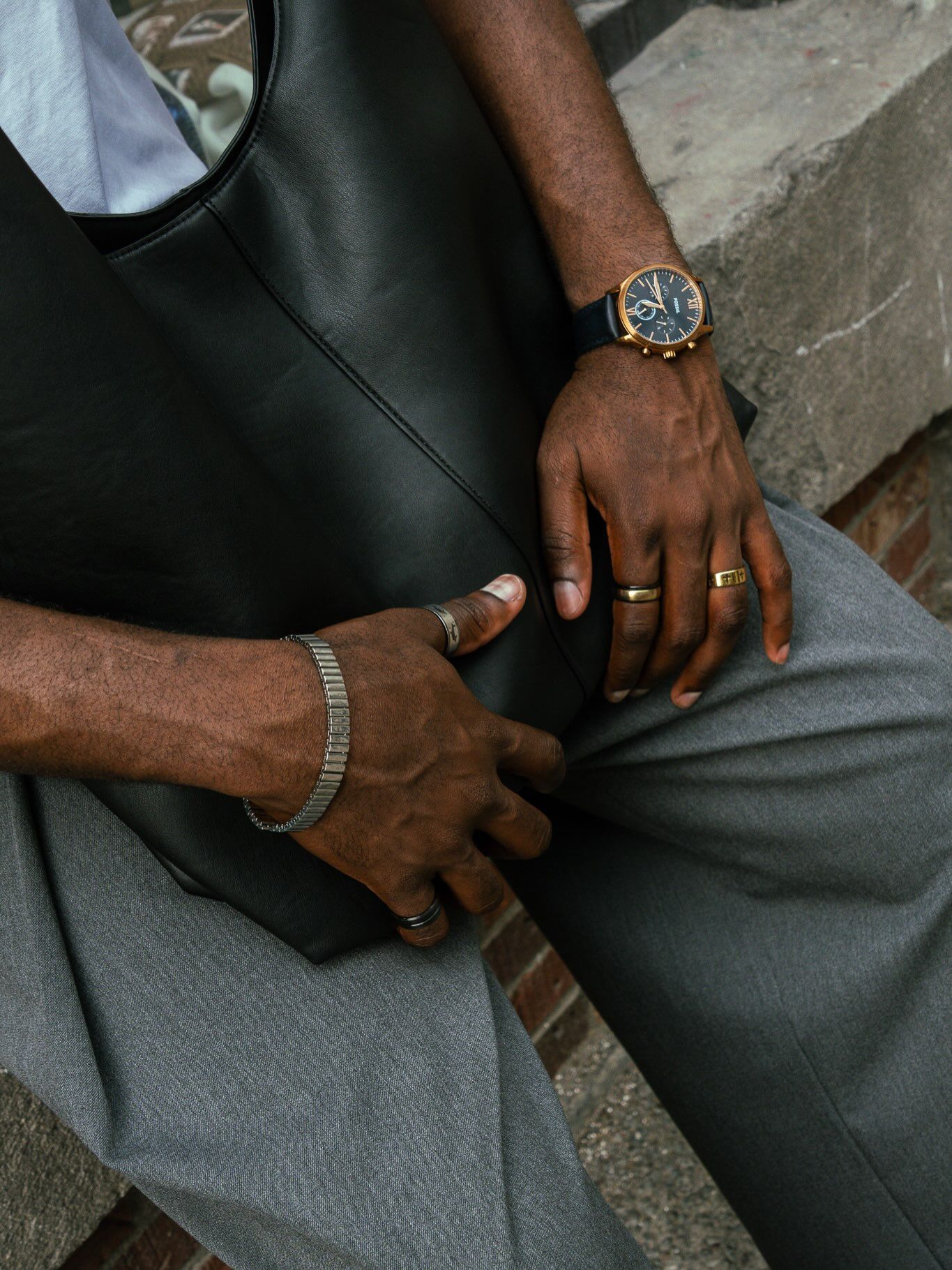 Détail : mains, montre et bracelets sur un pantalon gris