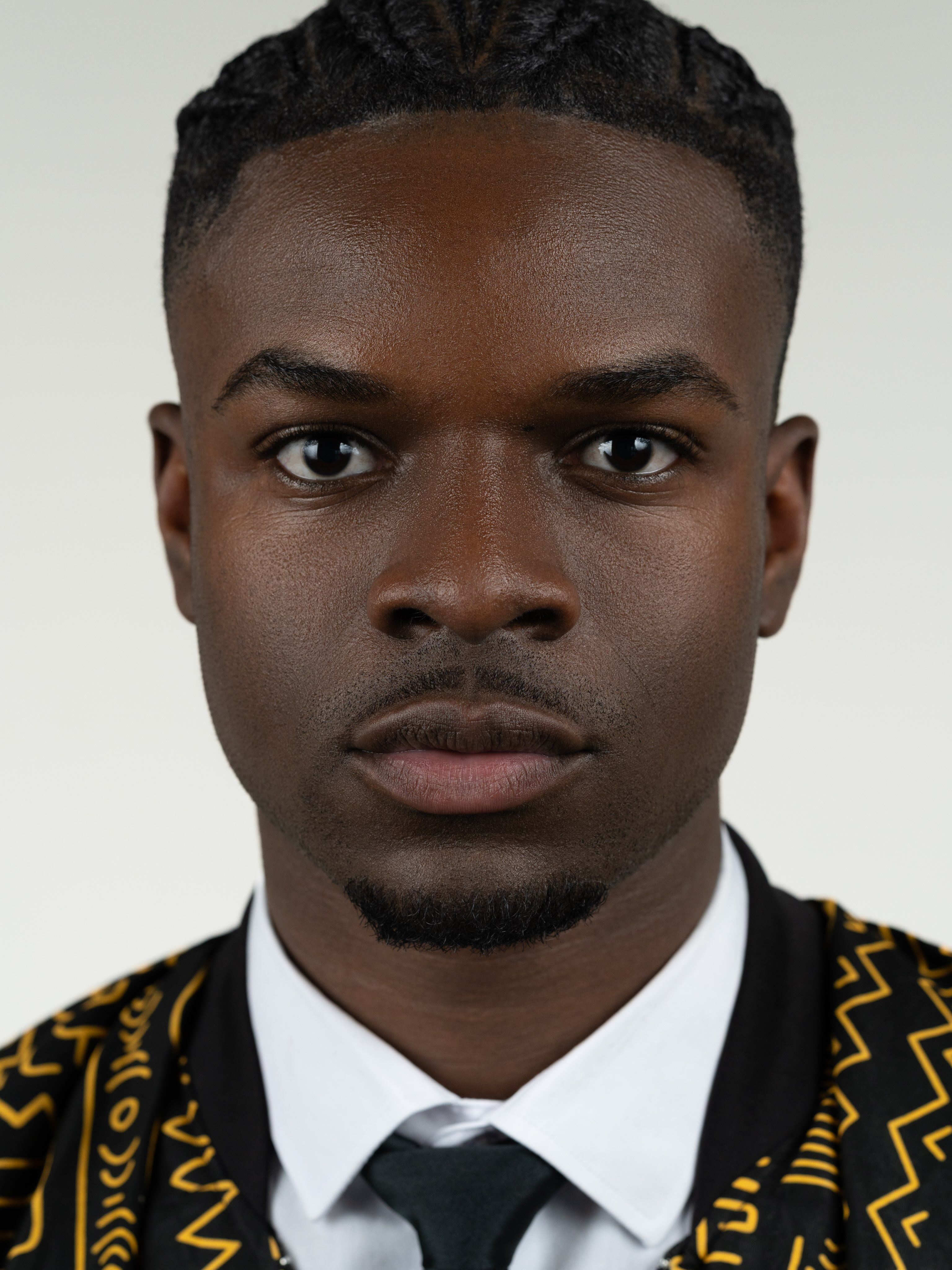 Portrait de Graël, regard droit vers la caméra, chemise blanche et cardigan à motifs